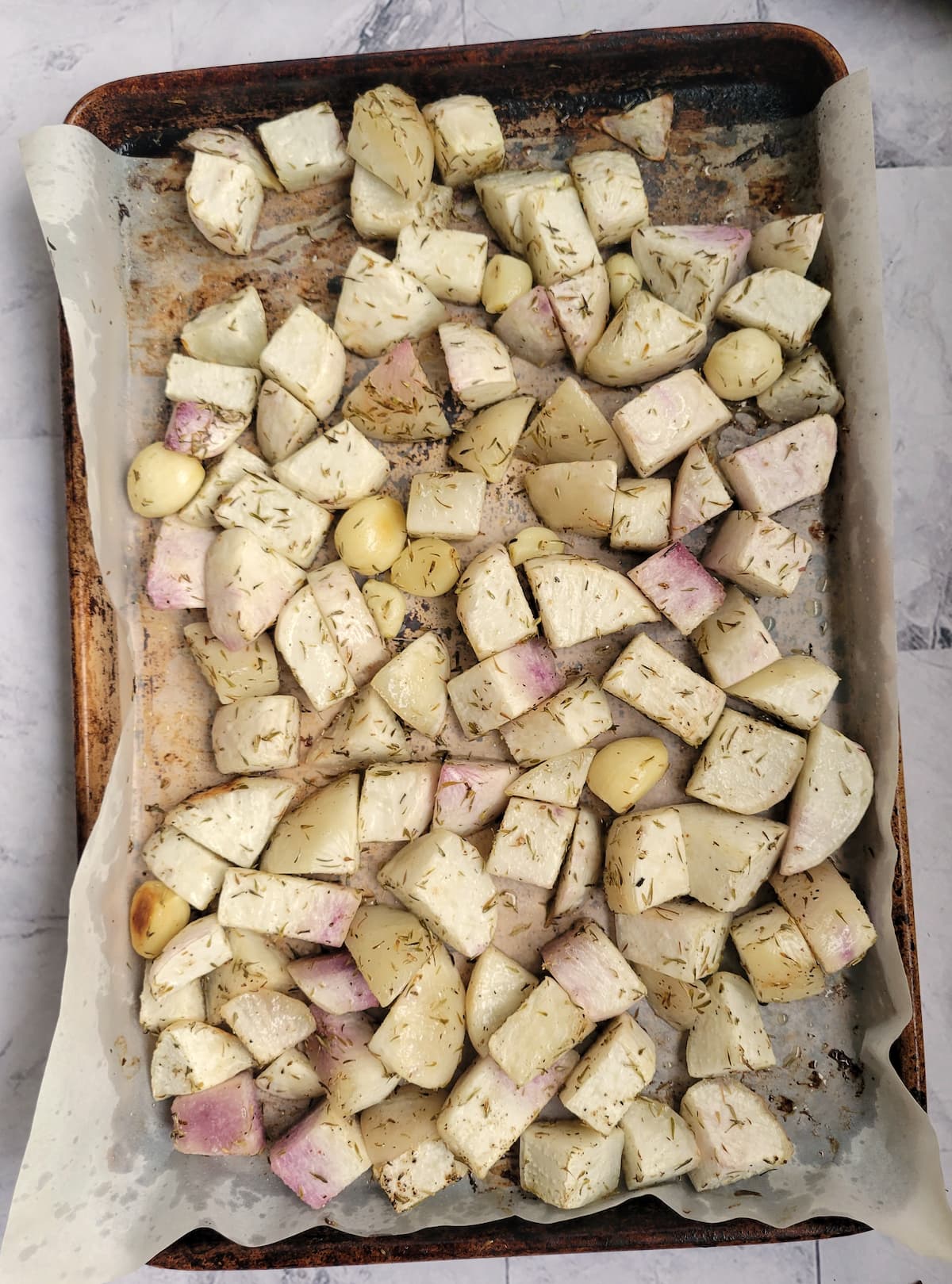parchment lined baking sheet with cubed seasoned turnips and whole garlic cloves