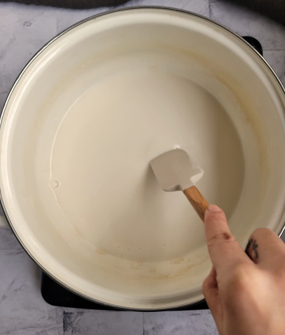 hand with a small rubber spatula in a pot of coconut milk