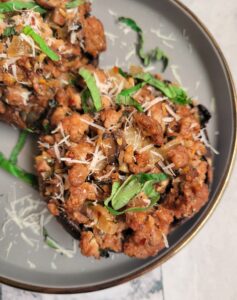 top view of 2 portobello mushrooms stuffed with cooked italian sausage, garnished with freshly grated parmesan cheese and fresh basil on a grey plate.