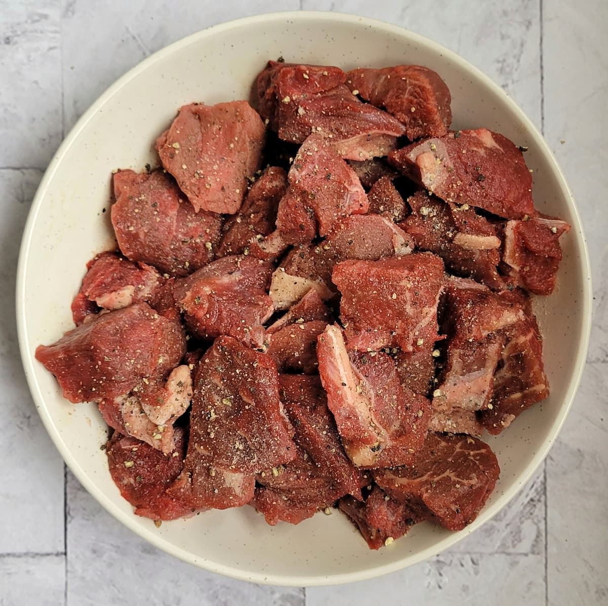 bowl of raw cubed beef seasoned with salt and pepper