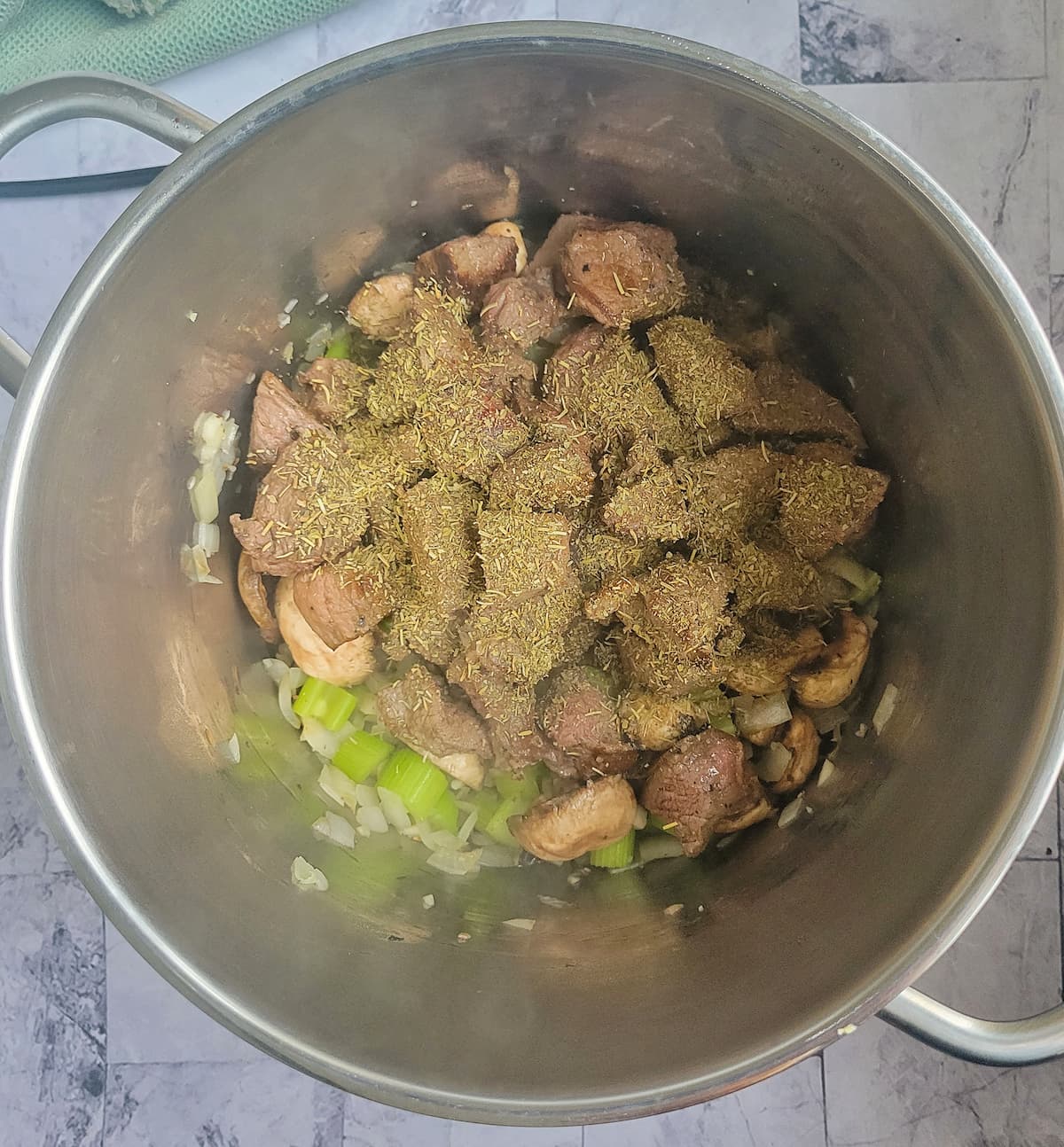 cubed beef with italian seasoning in a pot with some diced celery
