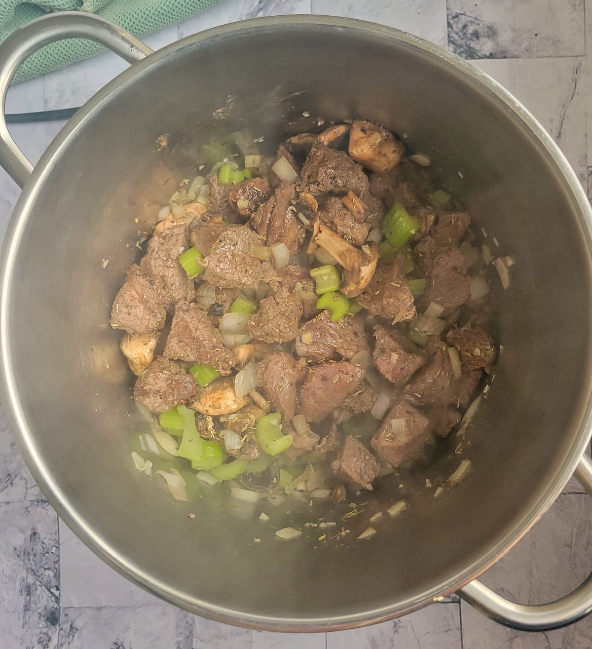 cubed beef in a pot with diced celery and onions