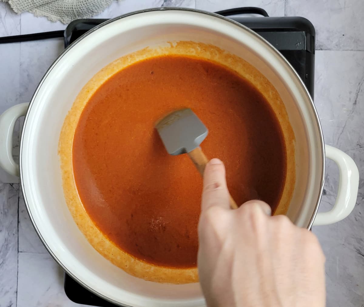 hand with a small rubber spatula stirring a pot of buffalo sauce