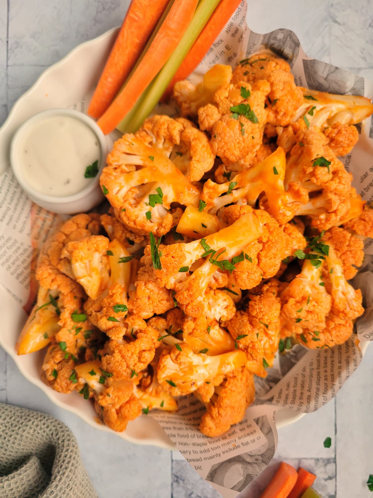buffalo cauliflower bites garnished with parsley, celery and carrot sticks on the side with a ramekin of blue cheese