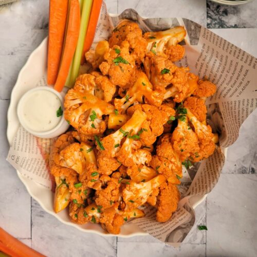 buffalo cauliflower bites garnished with parsley, celery and carrot sticks on the side with a ramekin of blue cheese
