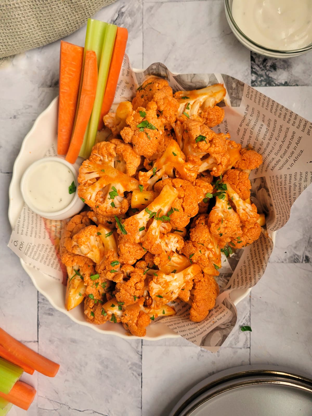 buffalo cauliflower bites garnished with parsley, celery and carrot sticks on the side with a ramekin of blue cheese
