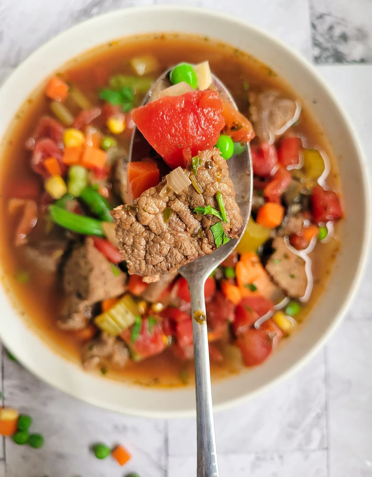 cooked beef cube with a diced tomato in a spoon over a bowl with the rest of it