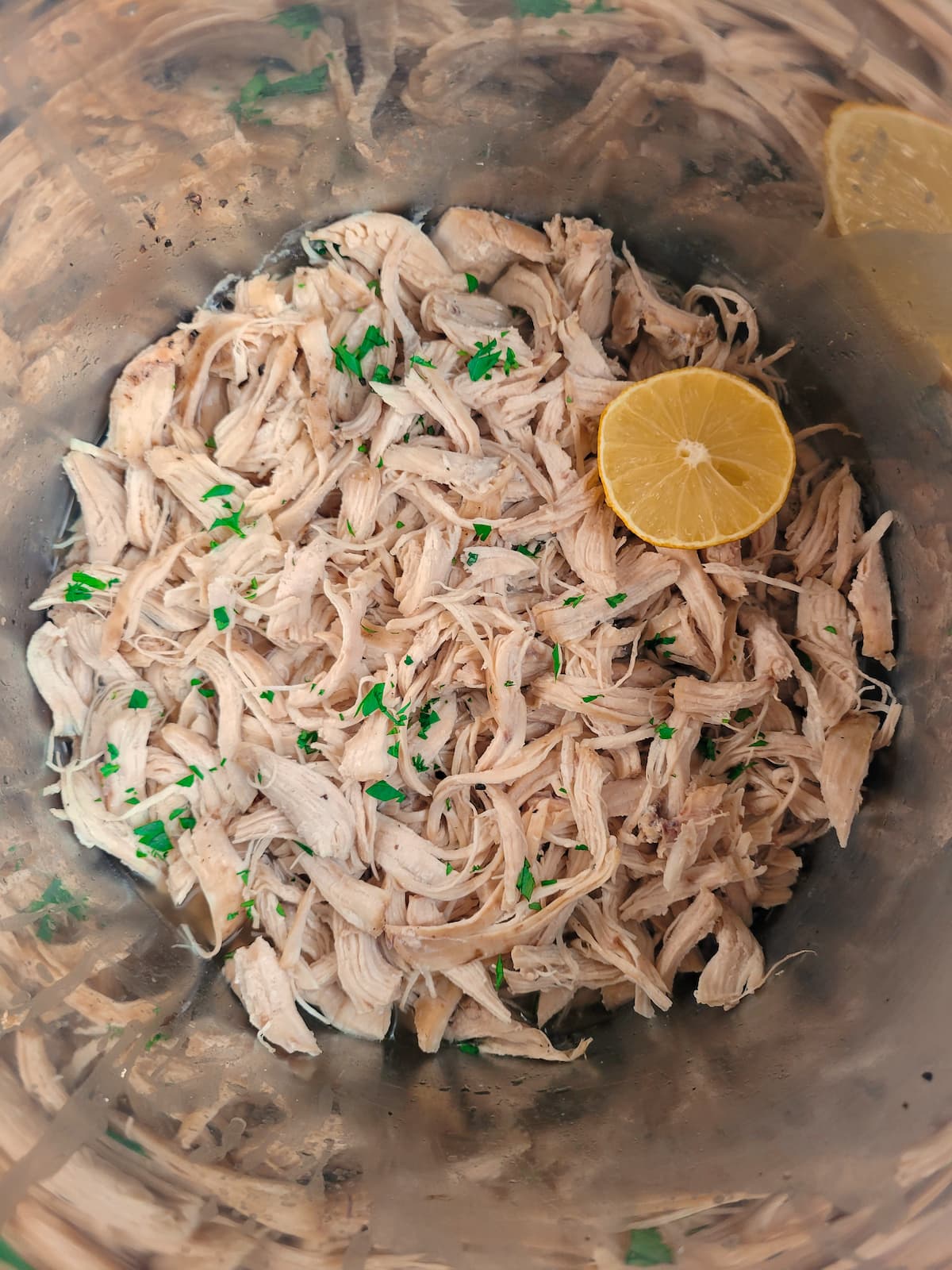 shredded chicken and lemon wedge in a pot garnished with fresh chopped parsley