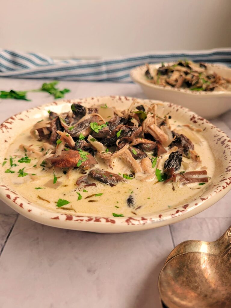 bowl of creamy mushroom and chicken soup garnished with fresh chopped parsley, another bowl of soup in the background, two spoons in the front