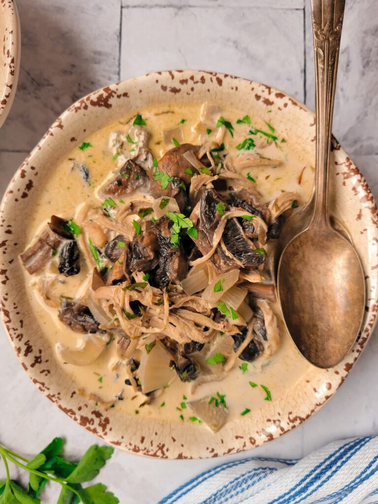 bowl of creamy mushrooms soup with shredded chicken, garnished with fresh parsley, two spoons in the bowl