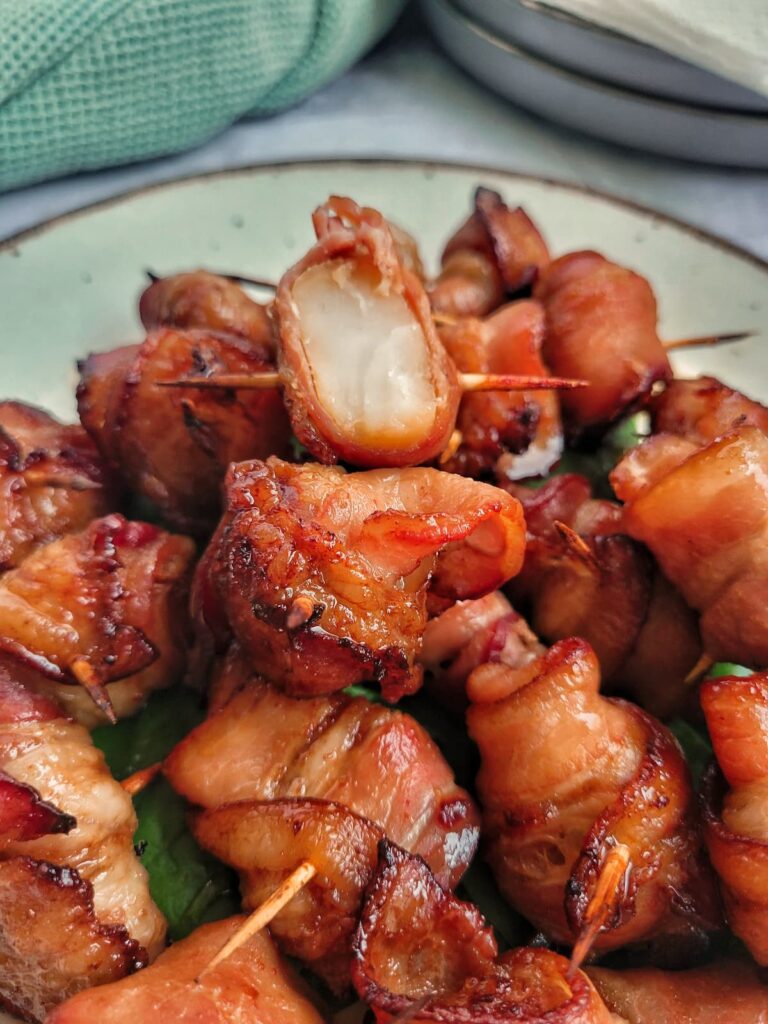 plate full of bacon wrapped water chestnuts with toothpicks in them, one half bitten on top