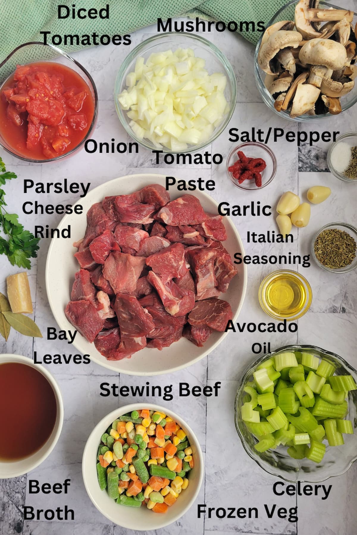 ingredients for beef with vegetable soup - stewing beef, frozen, veg, mushrooms, diced tomatoes, onions, tomato paste, salt/pepper, garlic, italian seasoning, avocado oil, celery, beef broth, cheese rind, bay leaves, parsley