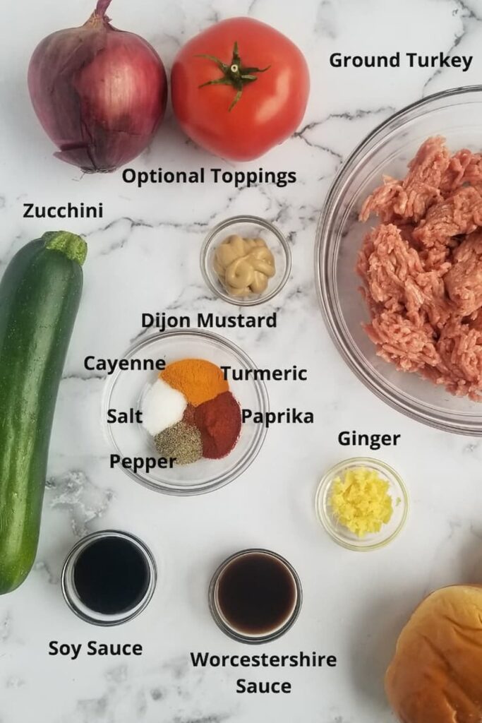 ingredients for zucchini turkey burgers - optional toppings (red onion, tomato), ground turkey, dijon mustard, minced ginger, salt, pepper, turmeric, paprika, cayenne, worcestershire sauce, soy sauce, zucchini