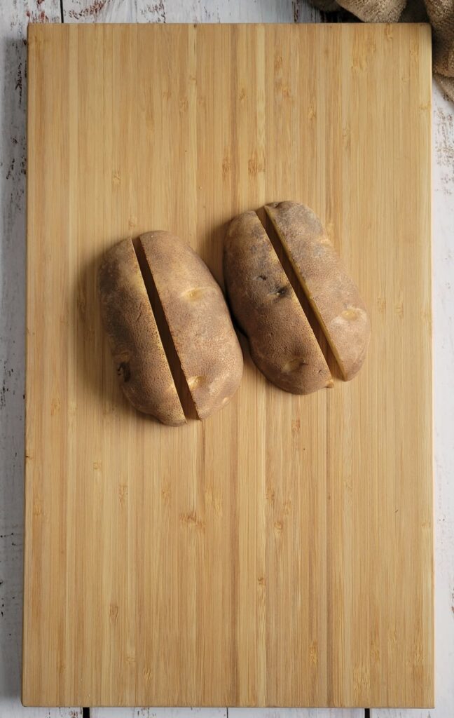 2 halves of a potato cut in half on a cutting board, face down