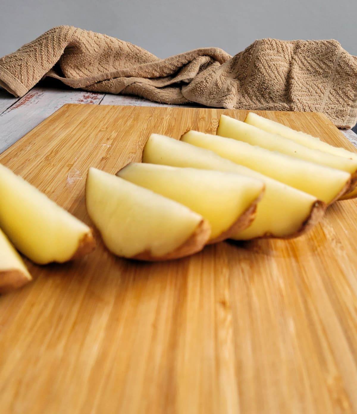 raw potato wedges lined up on a cutting board