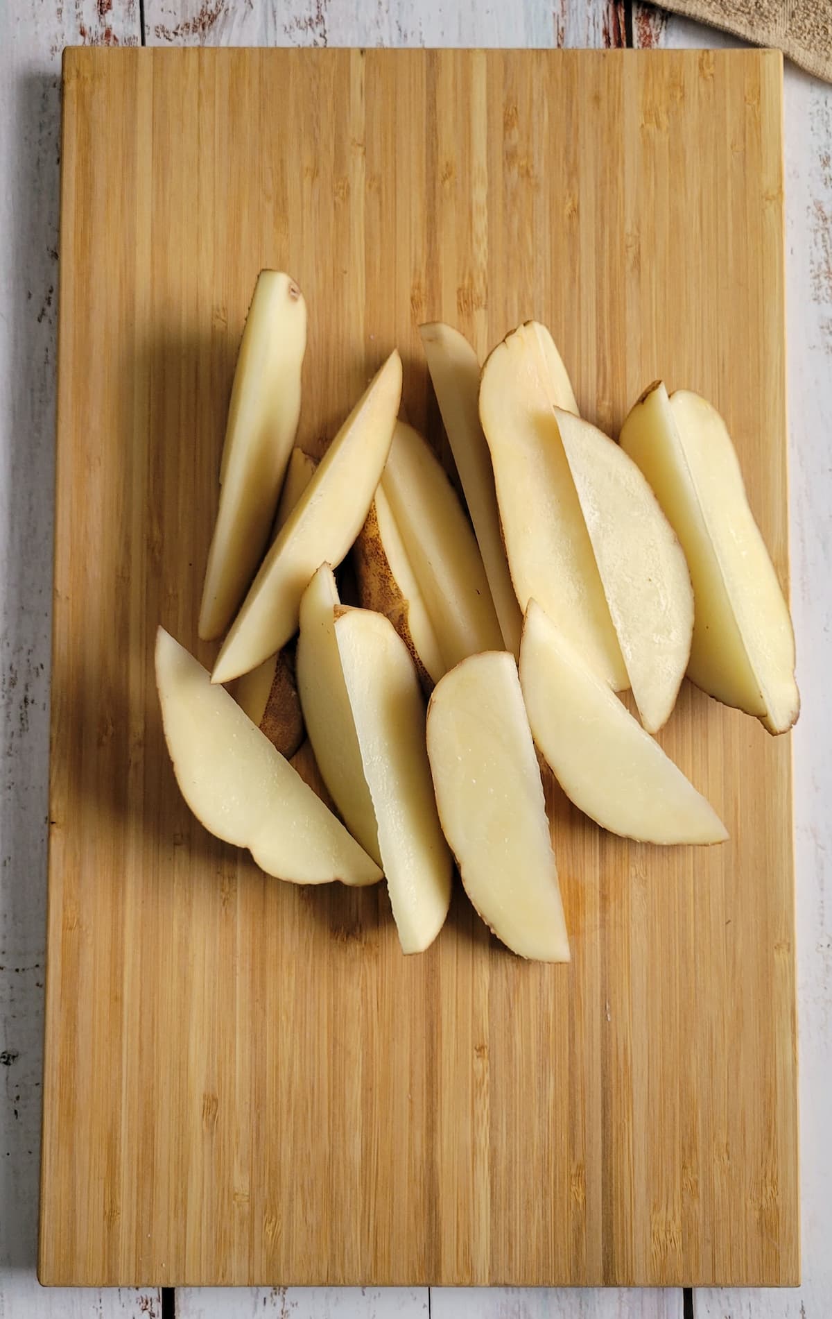 raw potato wedges in a pile on a cutting board