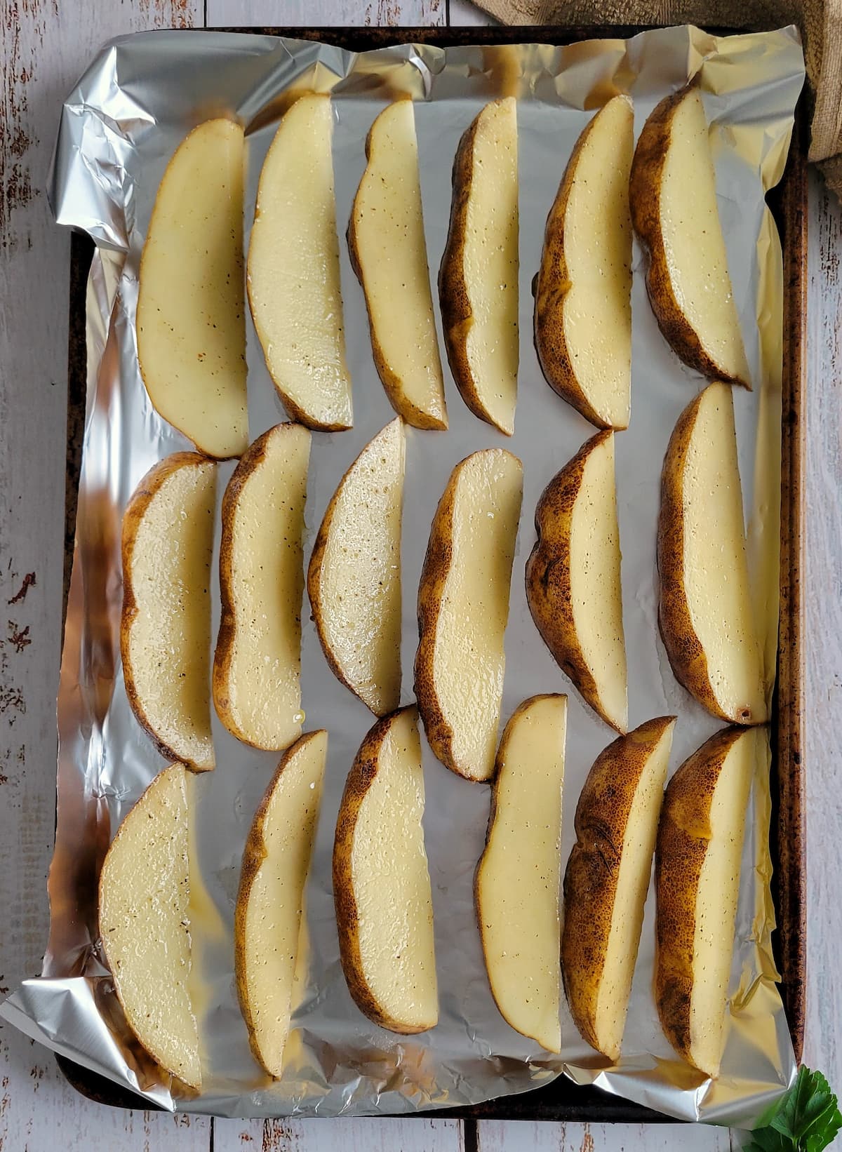 raw seasoned potato wedges in a single layer on an aluminum lined baking sheet