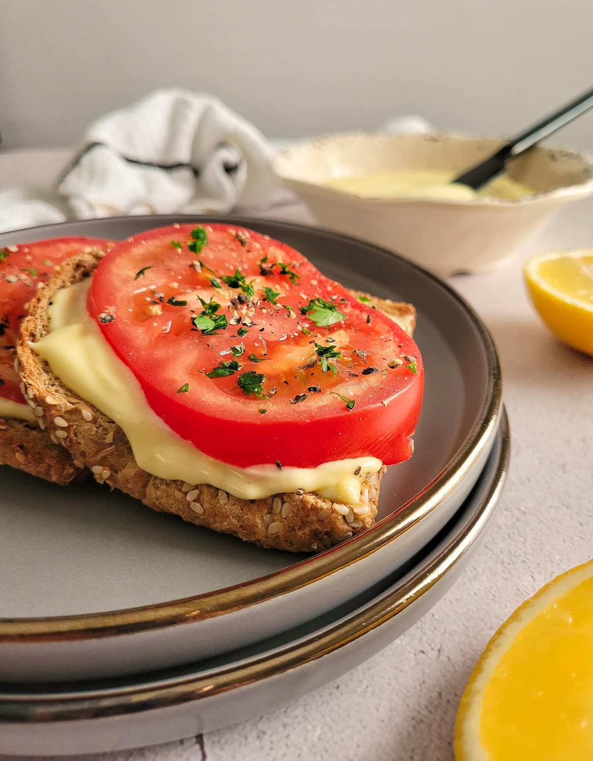 sliced tomato on toast with mayo and chopped parsley, bowl of mayo and lemon halves in the background