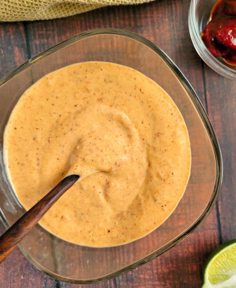 bowl of chipotle mayo with a spoon in it, half a lime and ramekin of chipotle peppers in the background