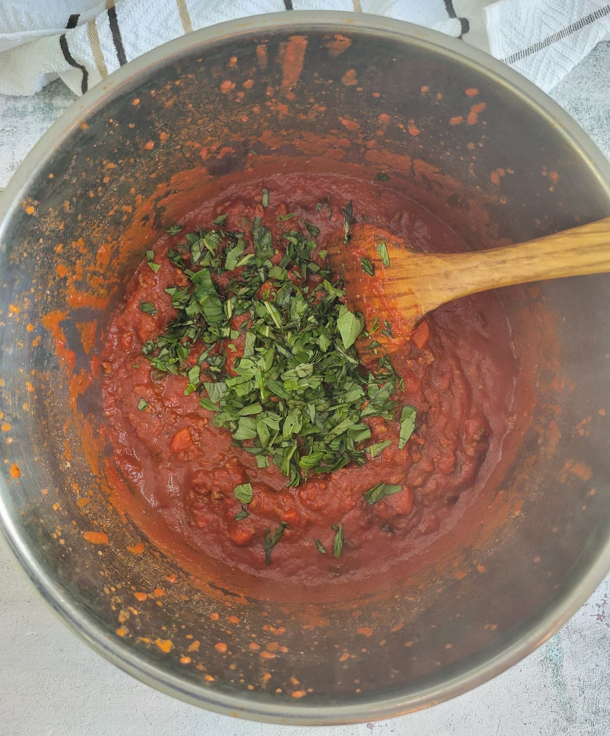 chopped fresh basil in a pot of tomato sauce with a wooden spatula