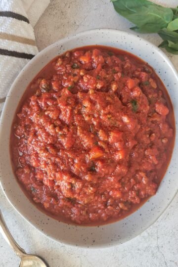 bowl of tomato and meat sauce, fresh basil in the background