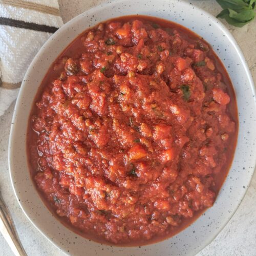 bowl of tomato and meat sauce, fresh basil in the background