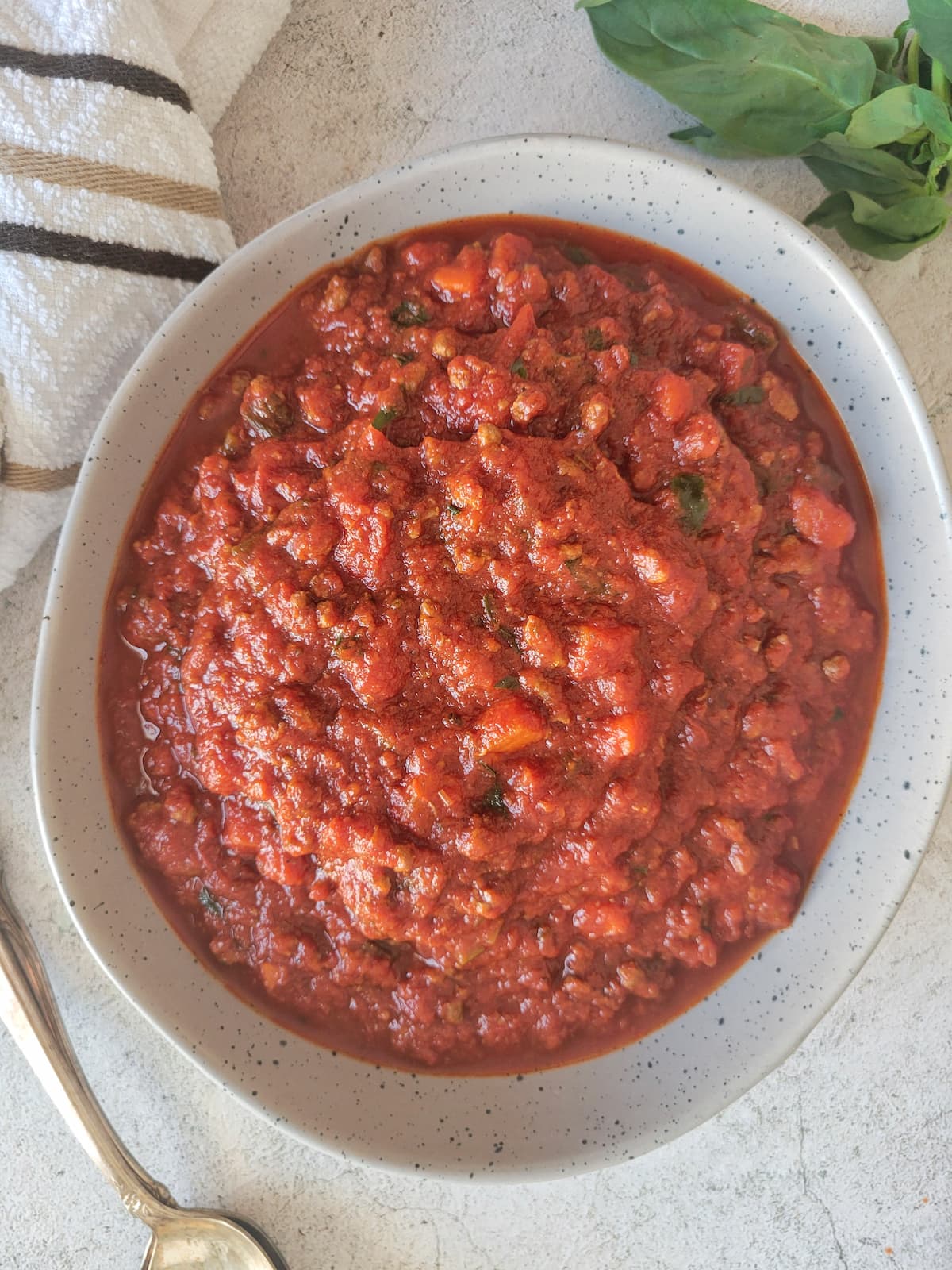 bowl of tomato and meat sauce, fresh basil in the background