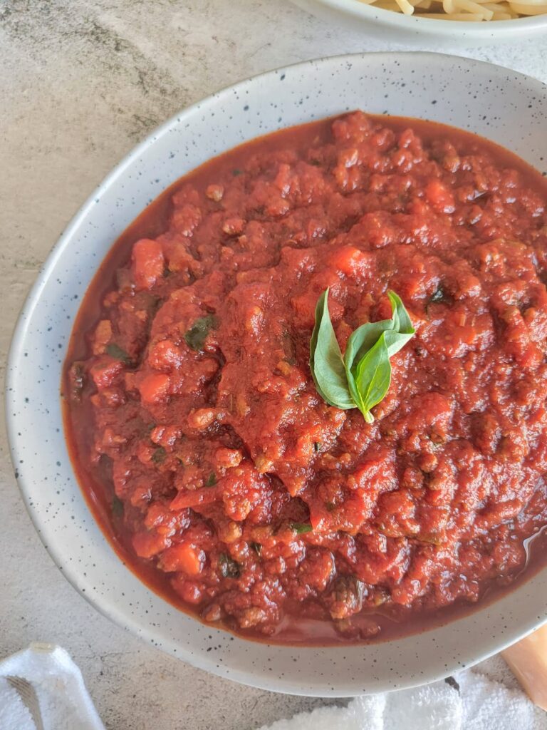 meat and tomato sauce in a bowl garnished with fresh basil