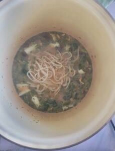 noodles in a pot with broth and bok choy