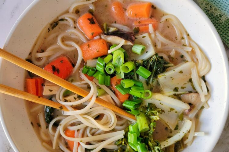 rice noodles in creamy brothy soup with green onions, bok choy, mushrooms and carrots, chopsticks in the bowl