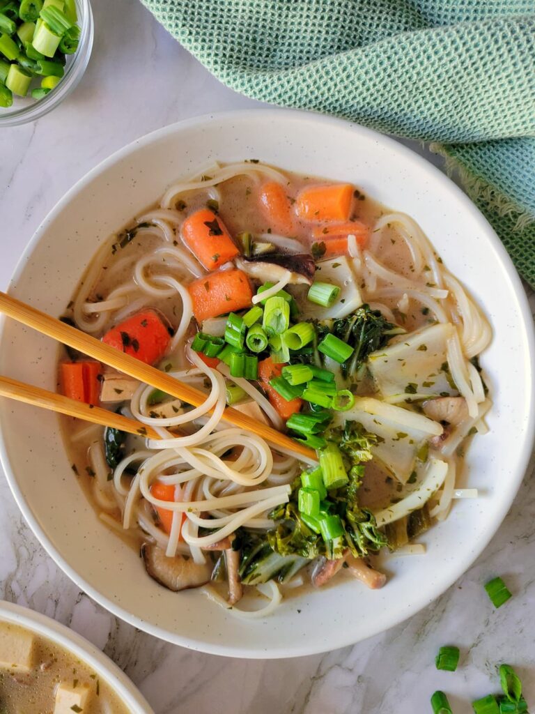 rice noodles in creamy brothy soup with green onions, bok choy, mushrooms and carrots, chopsticks in the bowl