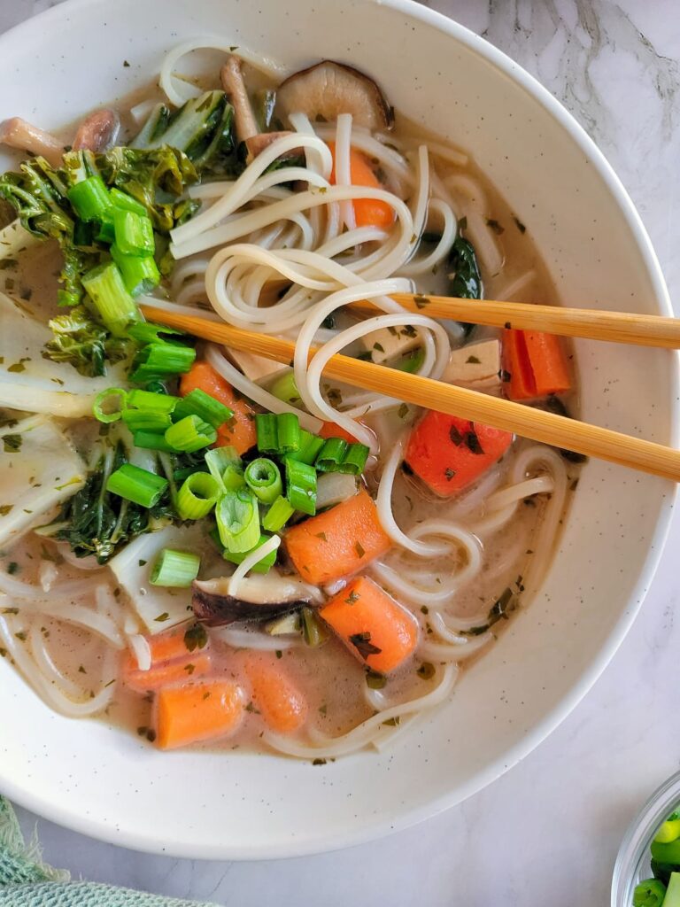 rice noodles in creamy brothy soup with green onions, bok choy, mushrooms and carrots