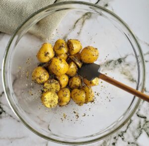 halved seasoned baby potatoes in a large glass bowl with a small rubber spatula