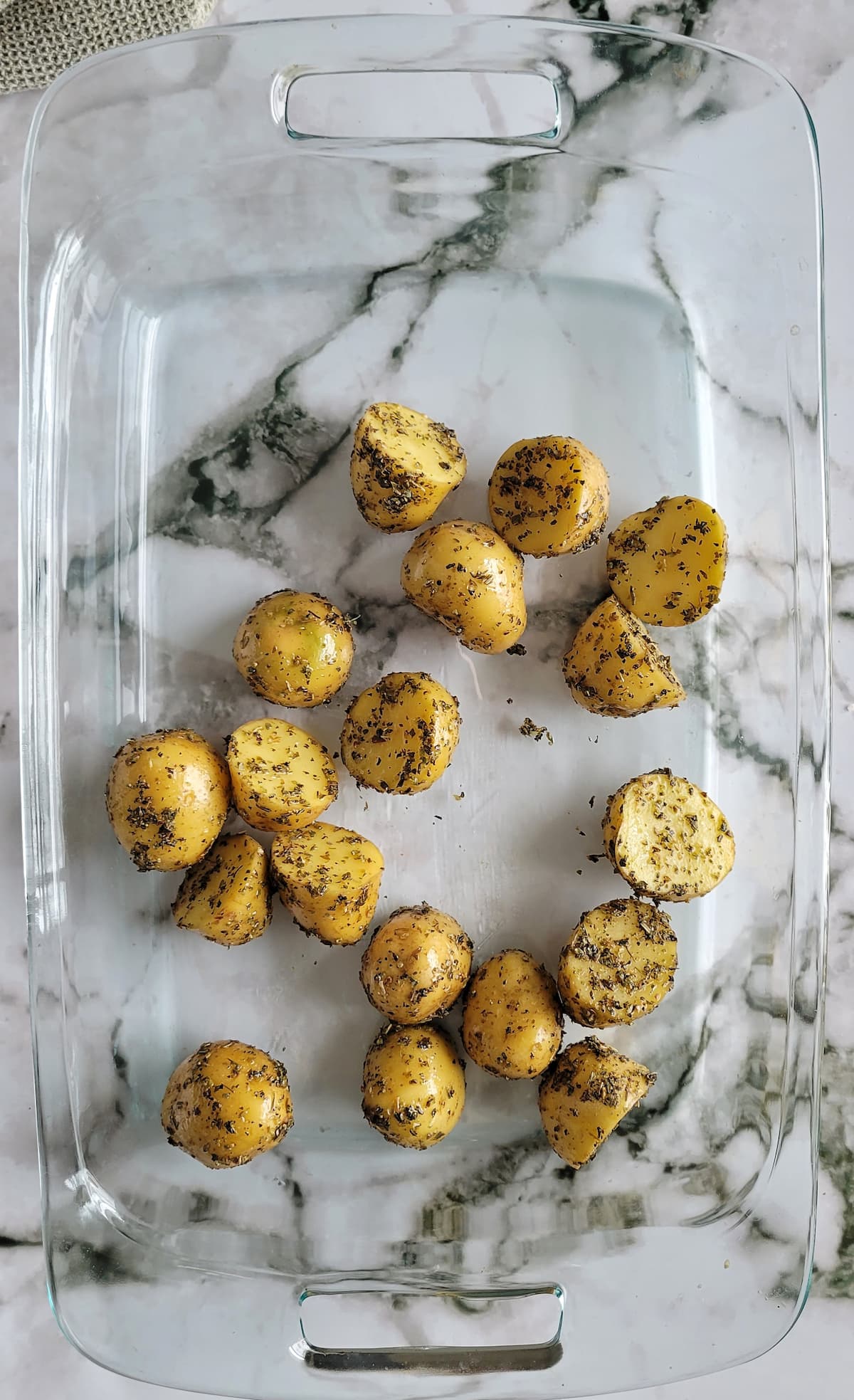 halved, seasoned baby potatoes at the bottom of a glass baking dish