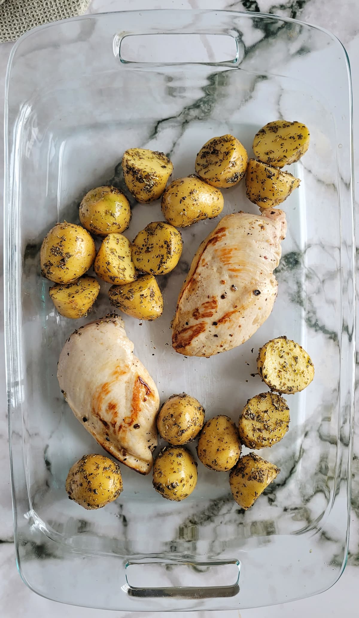 two seasoned chicken breasts and halved baby potatoes in a glass baking dish