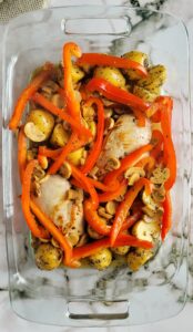 glass baking dish with two chicken breasts, baby potatoes, sliced mushrooms and red bell peppers