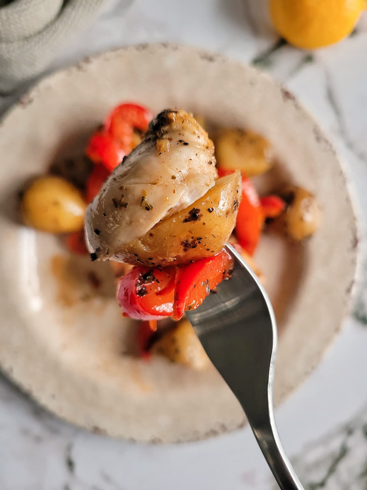 fork with some chicken, potato and red bell pepper over a plate with the rest