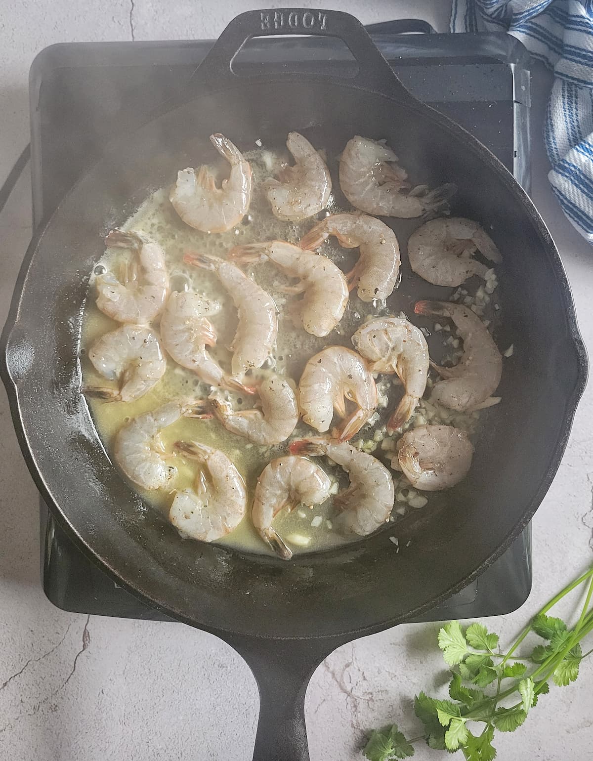 raw shrimp in a cast iron pan sauteeing in butter, garlic and oil