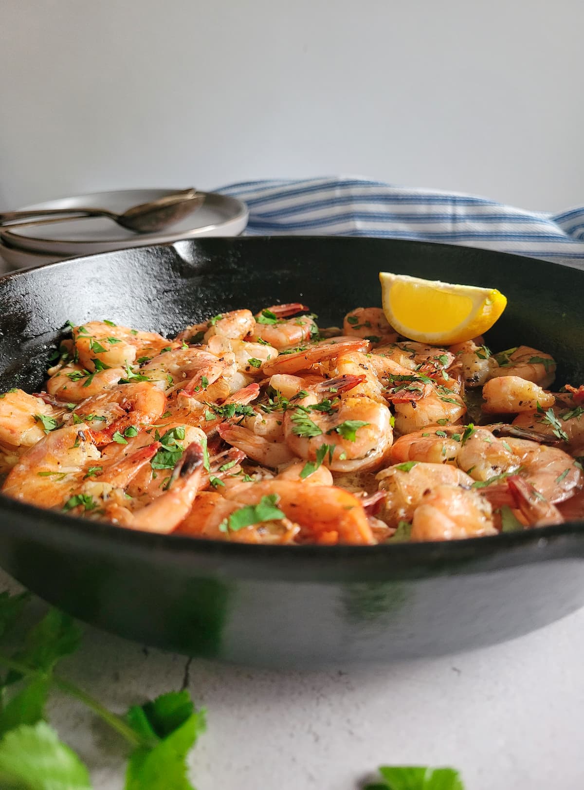 side view of sauteed shrimp in a cast iron skillet garnished with fresh chopped parsley and a lemon wedge
