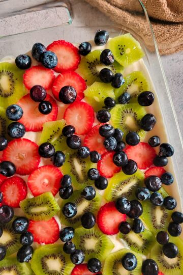 glass baking dish with a dessert with whipped cream and fresh sliced strawberries, kiwis and blueberries