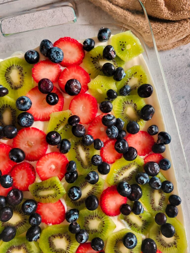 glass baking dish with a dessert with whipped cream and fresh sliced strawberries, kiwis and blueberries