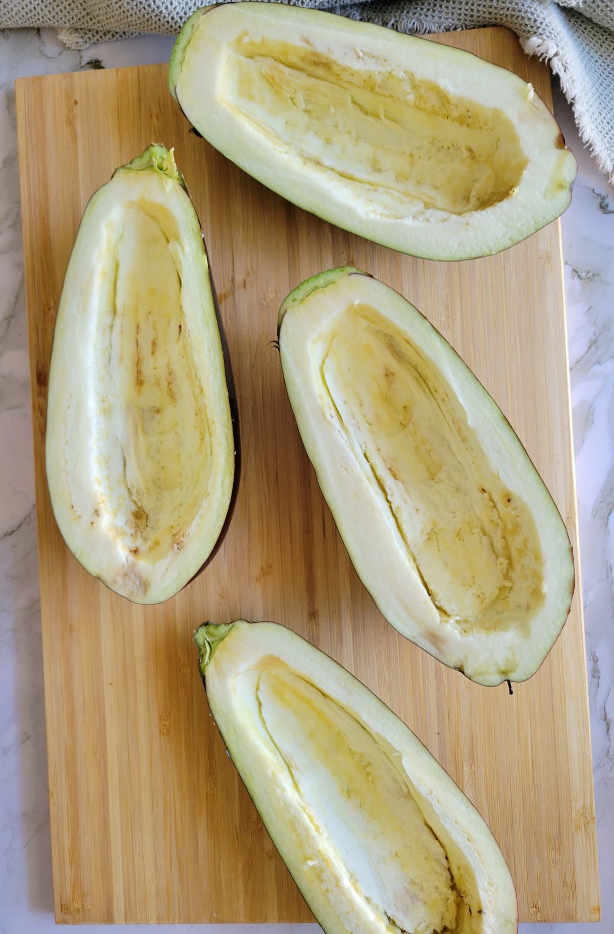 hollowed out eggplant halves on a cutting board