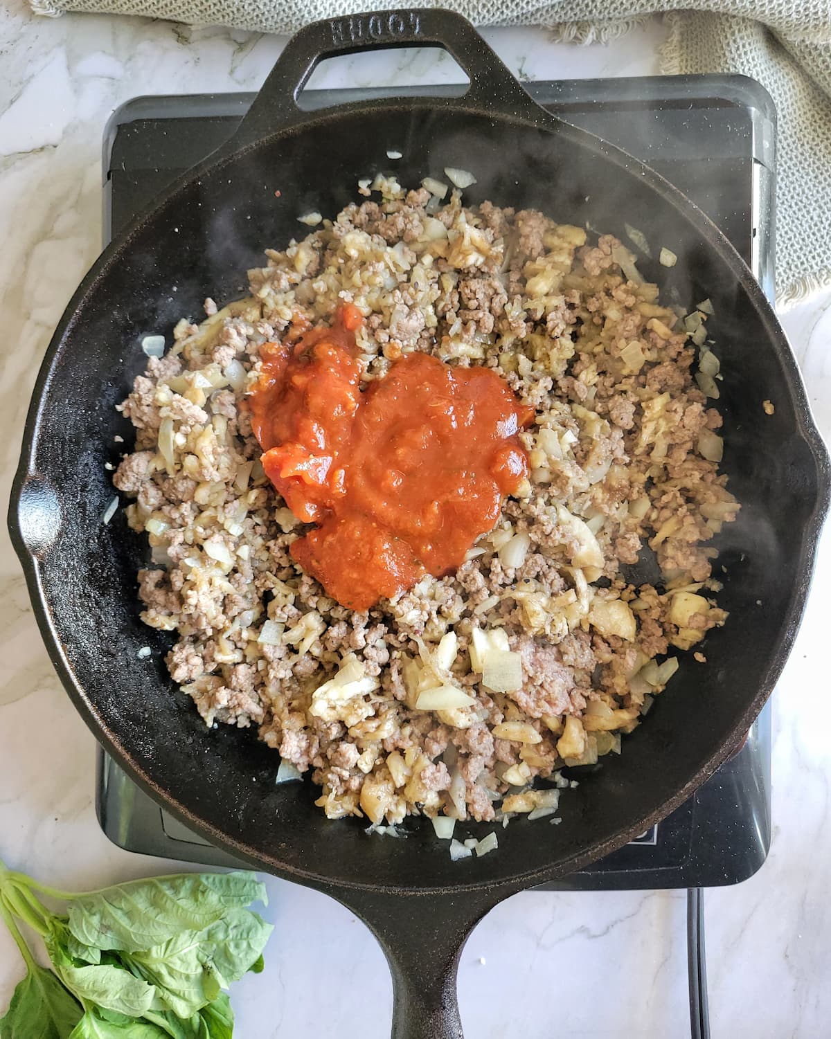 tomato sauce and ground beef simmering in a cast iron skillet