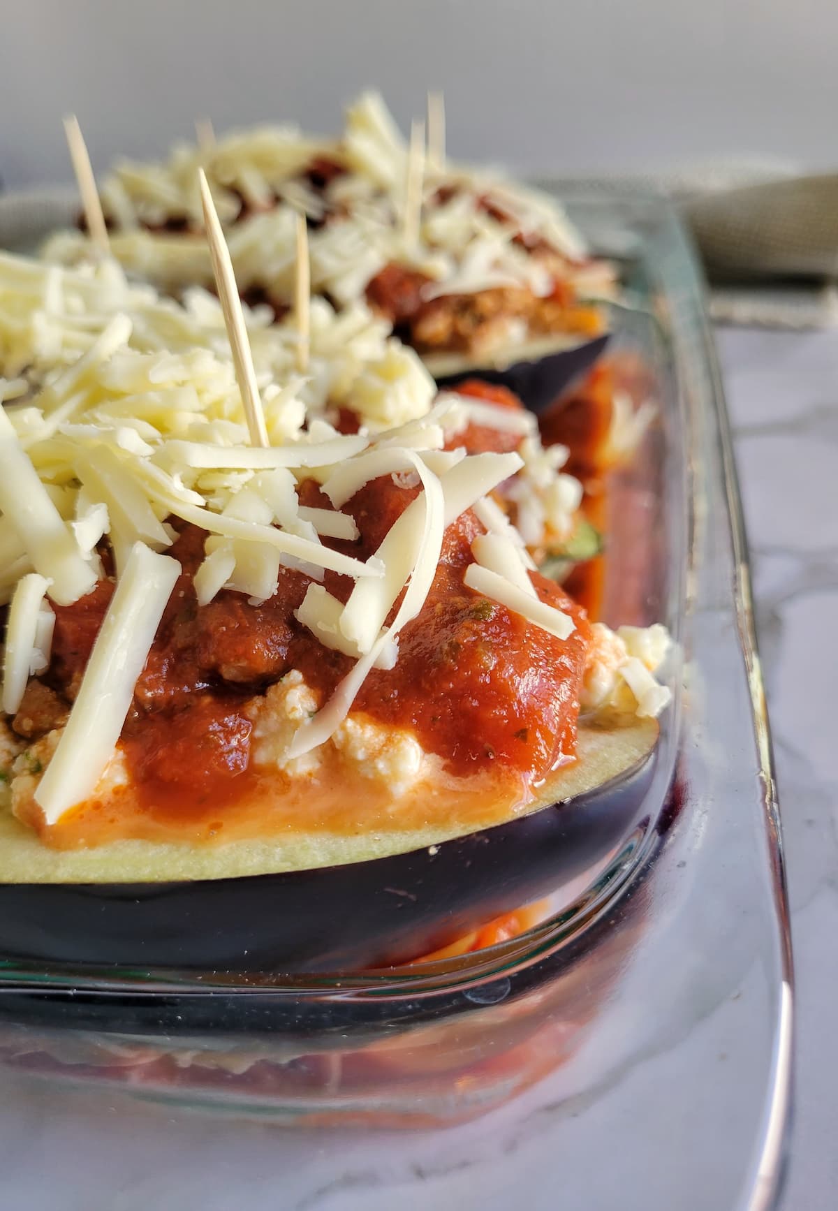 stuffed eggplant with mozzarella cheese in a rectangular baking dish, toothpicks in the eggplant