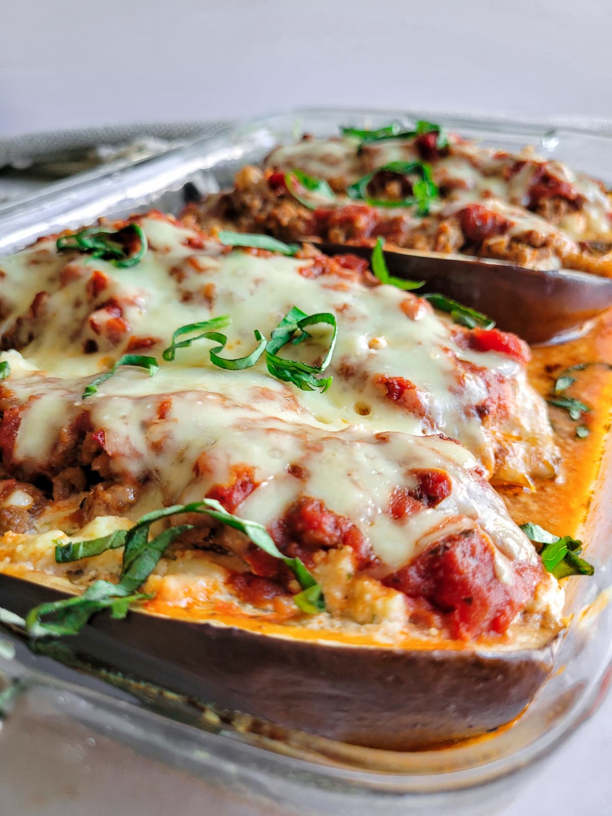 lasagna stuffed eggplant in a baking dish topped with fresh chopped basil