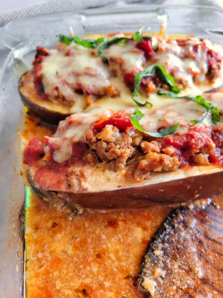 lasagna stuffed eggplant in a baking dish topped with fresh chopped basil