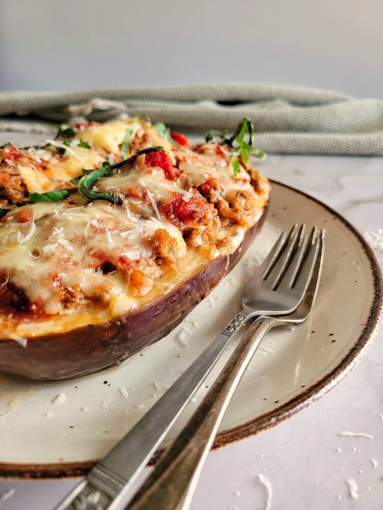 lasagna stuffed eggplant garnished with fresh chopped basil and freshly grated parmesan cheese on a plate with two forks