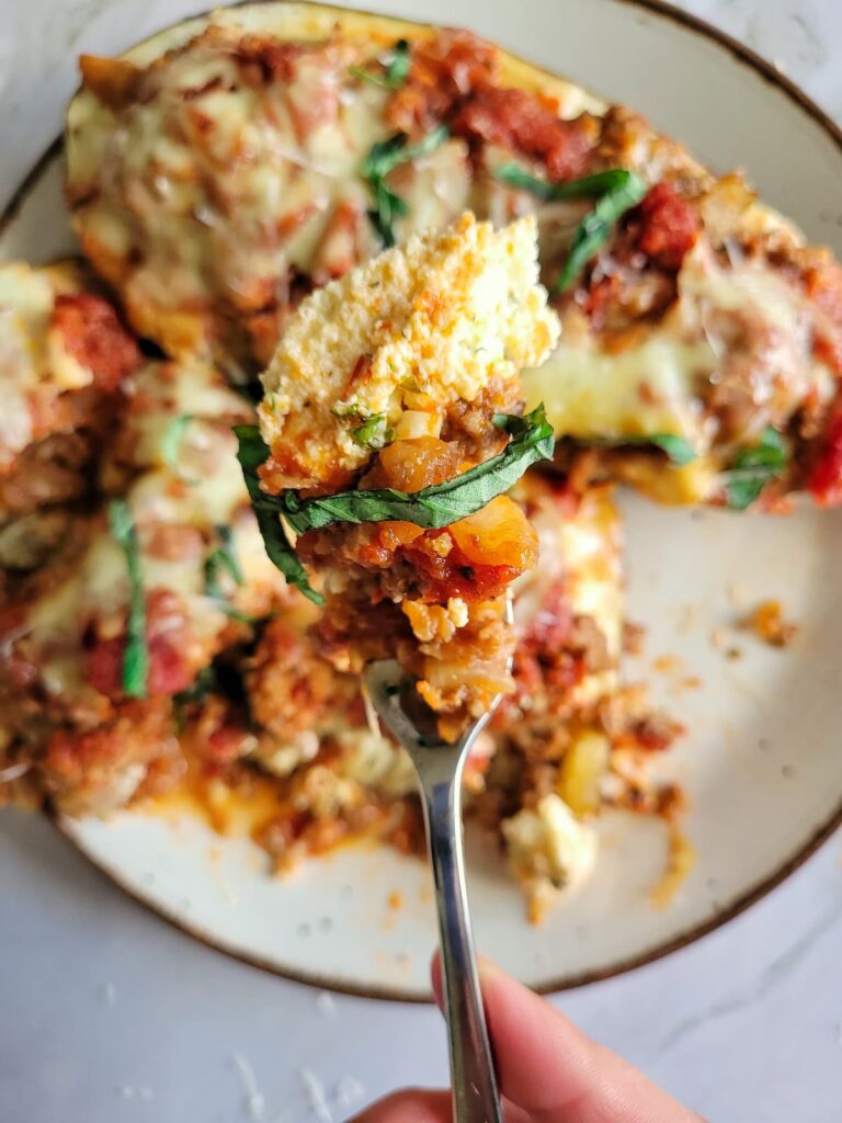 fork with some ricotta and fresh basil, ground beef and tomato sauce over a plate of lasagna stuffed eggplant