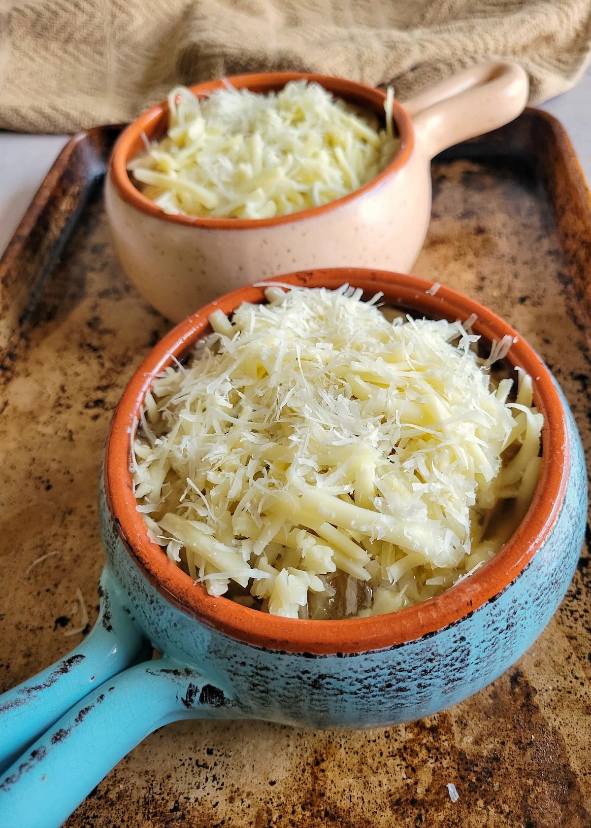 two bowls of french onion soup with unmelted cheese on a sheet pan