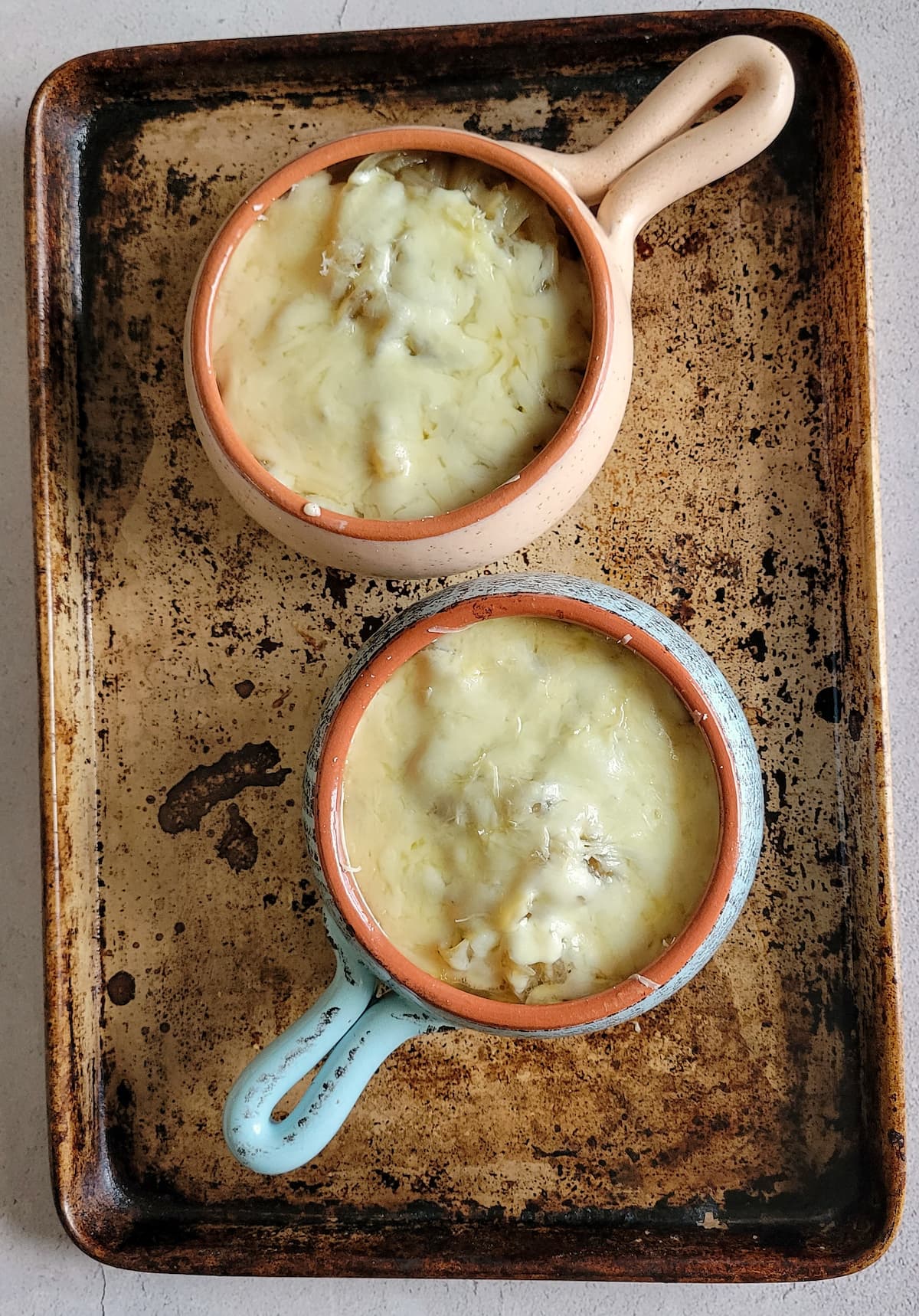 two bowls of french onion soup with melted cheese on a sheet pan